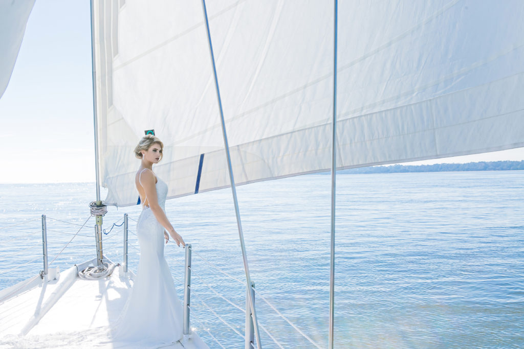 Bride standing at bow of sailboat on the ocean