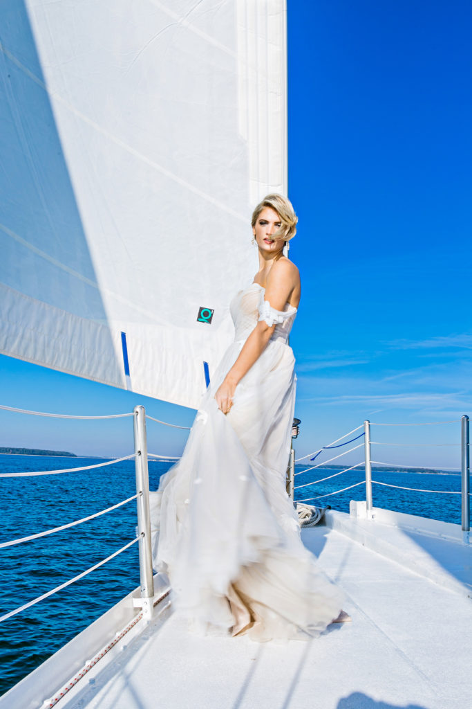 bride standing on bow of sailboat in a wedding dress